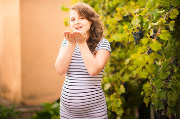 A beautiful pregnant girl stands in a vineyard and sends an air kiss.