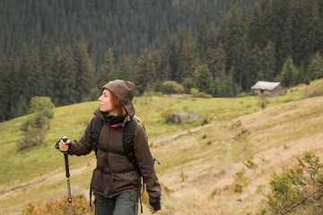 Female hiker with backpack walking on the mountains roads, autumn forest background 