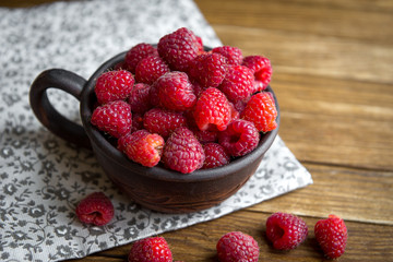a ceramic mug with raspberries and a bowl with blackberries stand on a wooden table.
