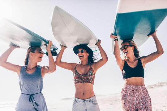 Happy young adult friends having fun at the beach surfing