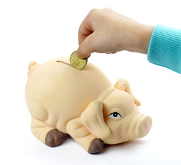 woman hand dropping coin in piggy bank against white