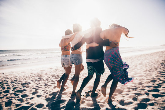 Happy group of young adult friends walking on the beach together