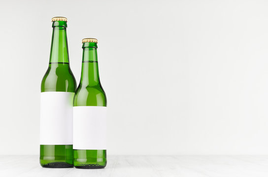 Green beer bottles longneck 500ml and 330ml with blank white label on white wooden board, mock up. Template for advertising, design, branding identity.