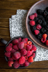 a ceramic mug with raspberries and a bowl with blackberries stand on a wooden table.
