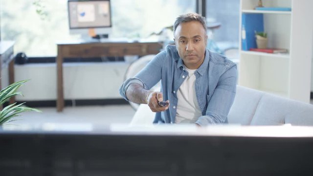 Cheerful Asian man watching TV at home and channel surfing