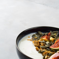 Healthy breakfast natural yogurt bowl with home made granola, pumpkin seeds and figs on gray background