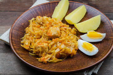 Stewed cabbage with meat is served with egg and potatoes on a clay plate. Traditional European food.