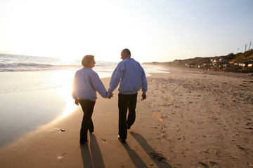 Elderly couple holding hands and walking on the beach