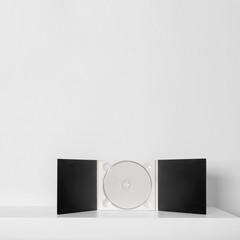 Listen to the music, white cd in lack case on the shelf near the white wall