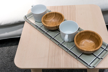 Small empty white mug and wooden bowl arranged in grey tray on wooden side table