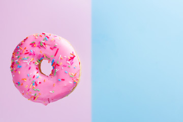 one falling sweet doughnut on blue and pink background with copy space