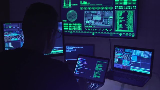 Male hacker working on a computer in a dark office room.
