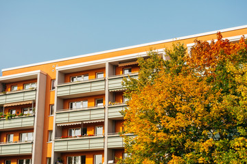 orange plattenbau building with white balcony and autumn tree
