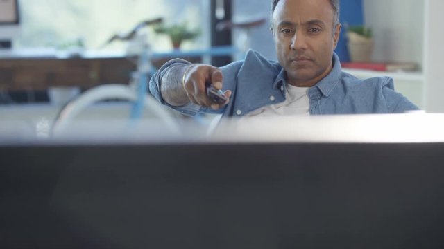 Cheerful Asian man watching TV at home and channel surfing