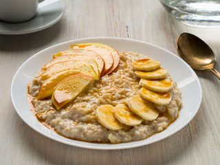 Healthy Breakfast in the morning - oatmeal with fruit and honey, slices of apples and bananas, caramel syrup.  Selective focus