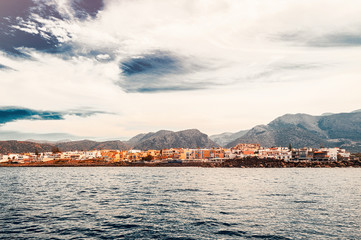 View from the sea to mountain coast. Low-rise buildings with red roof. Lovely summer landscape.