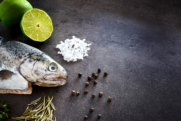 Fresh rainbow trout with lime and seasoning. Fish at dark background. Detail of preparation - 178052304