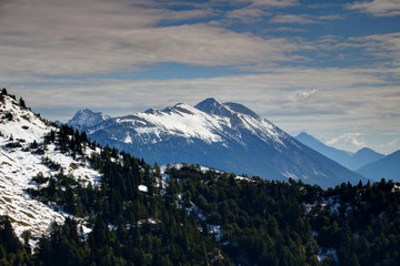 Fototapeta na wymiar Snow-capped Stol / Hochstuhl, highest peak of Karavanke / Karawanken mountain range, with pine forests on steep slopes, on the border of Austria and Slovenia, Europe