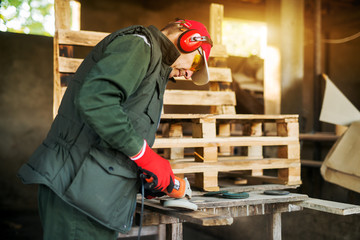 Rear view of senior carpenter burning wood with electric grinder tool in a professional uniform.