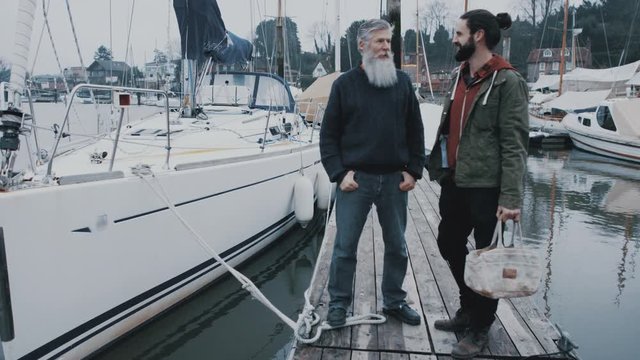  Portrait smiling bearded men standing in front of sailing boat in a marina