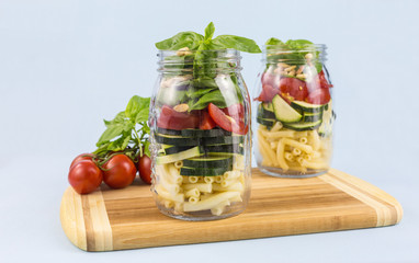 layered vegetable salad with pasta, zucchini, tomato, basil leaves and pine nuts