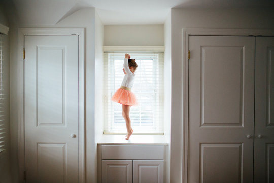 little girl doing ballet in a tutu on a window seat