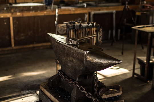 A metal anvil sits in a blacksmith workshop with a hammer on top