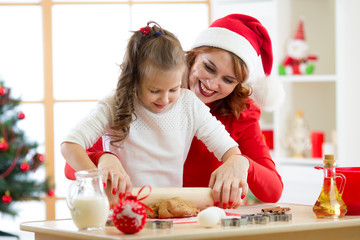 Happy woman and child girl stretching the christmas cookie dough together