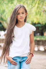 Fototapeta premium Beautiful school girl with long hair in the park. Prety Girl with a model appearance and with fashionable poses. Child of 8 years.