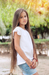 Fototapeta premium Beautiful school girl with long hair in the park. Prety Girl with a model appearance and with fashionable poses. Child of 8 years.