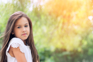 Naklejka premium Beautiful little girl in the park, with long hair and and a sweet, gentle look. Happy childhood concept.