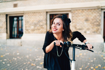 portrait of beautiful girl smiling and riding electric scooter. Autumn details in modern city, urban landscape
