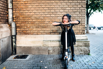Fototapeta na wymiar Happy woman using kick scooter in city - portrait against vintage brick wall. Technology eco transportation concept
