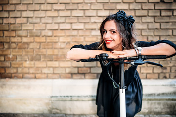 Close up portrait of beautiful woman using eco transportation. Portrait of happy smiling girl against brick wall