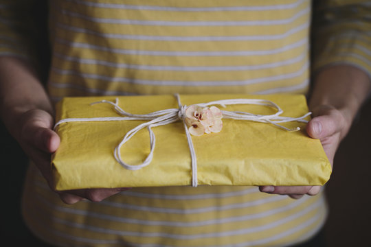 Hands holding a gift wrapped in yellow paper