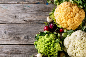 Variety of fresh raw organic colorful cauliflower, cabbage romanesco and radish with bundle of coriander over old wooden background. Top view with copy space. Food farm market concept
