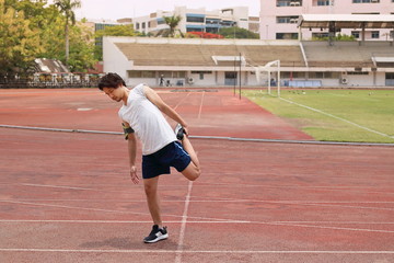 Young healthy Asian runner warming up before run on track in stadium. Vintage toned image.