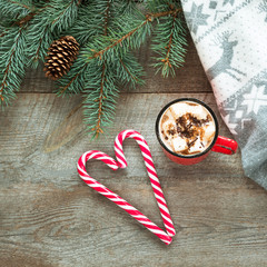 Christmas card. Cup of coffee with marshmallow, red candy cane in shape of heart on the wooden background. Top view.