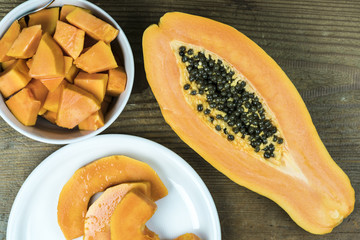 High angle view of papaya cut in half with small pieces in bowl against wooden background