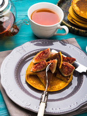 Eating pumpkin pancakes with figs and honey with hot tea. Autumn food background on green wooden table