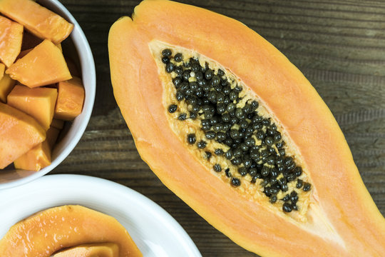 High angle view of papaya cut in half with small pieces in bowl against wooden background