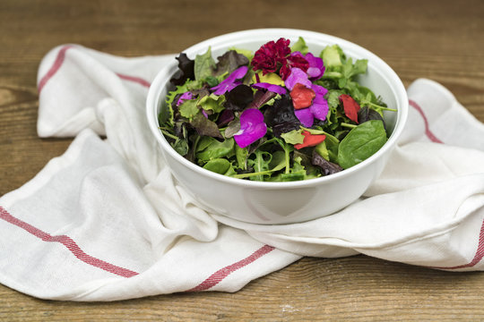 Bowl of mixed salad with edible flowers standing on dishcloth
