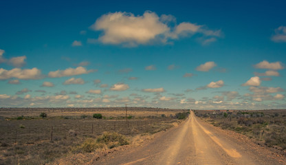 A dry dusty dirt road leads straight to the horizon in the arid Karoo area of South Africa