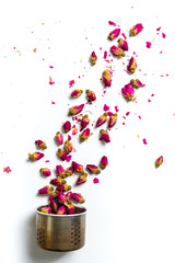 Obraz premium Rose tea flowers flying out of kettle colander on white