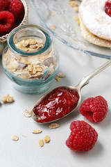 Spoon of sweet jelly, jar of muesli and raw raspberries.