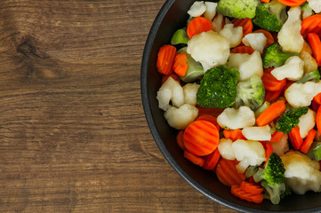 Mixed vegetables. cauliflower, broccoli and carrots in an iron pan on a wooden background. with copy space. top view