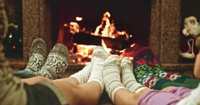 Feet in woolen socks warming by cozy fire in Christmas time in slow motion. Family with two kids warming their feet by the fireplace in winter time. Filmed at 120 fps 4k graded from RAW