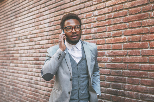 Cute black businessman on phone in front a brick wall.