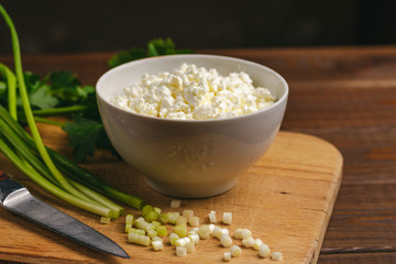 Cottage cheese in bowl and fresh herb on wooden board on table. Healthy food