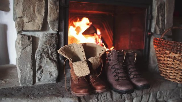 Couple Winter Boots Drying in front of a Burning Warm Fireplace - 4K. Family vintage folk boots getting warm near the fireside in a cabin. Warm cozy fireplace in the authentic chalet. 